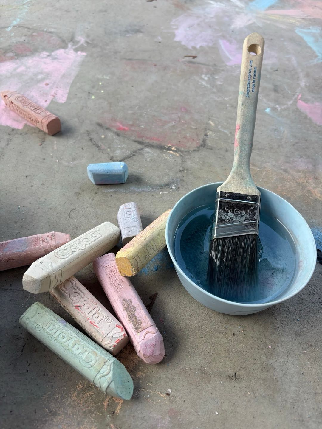 Sidewalk chalk beside a paintbrush in a bowl of water